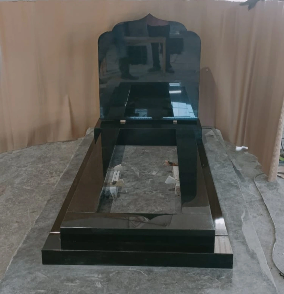 Polished black memorial with a shaped, pointed headstone and straight kerb surround, shown in the workshop.