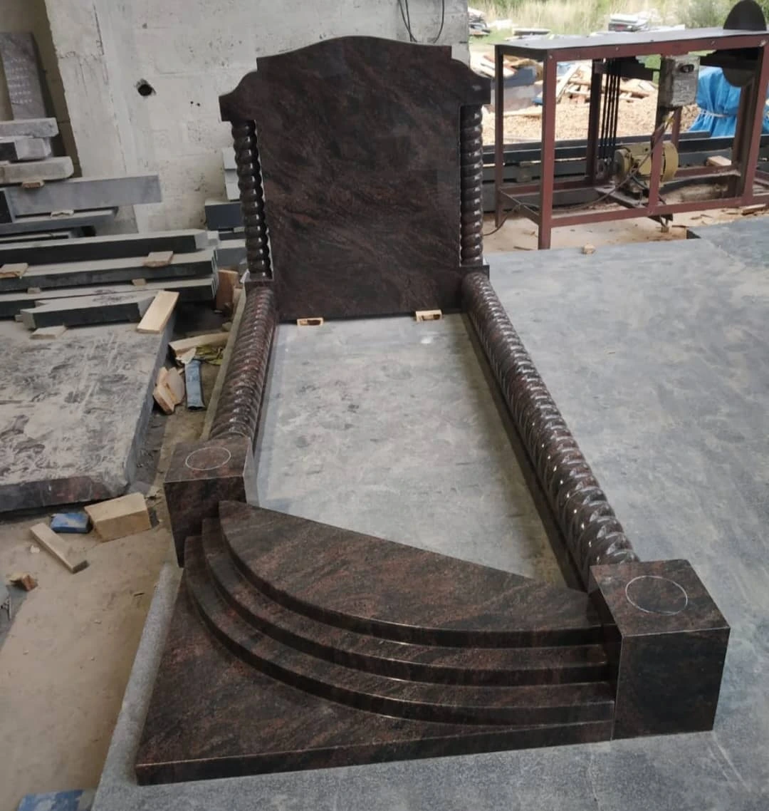 Dark veined memorial with decorative side rails and a curved, stepped foot, shown in the workshop.