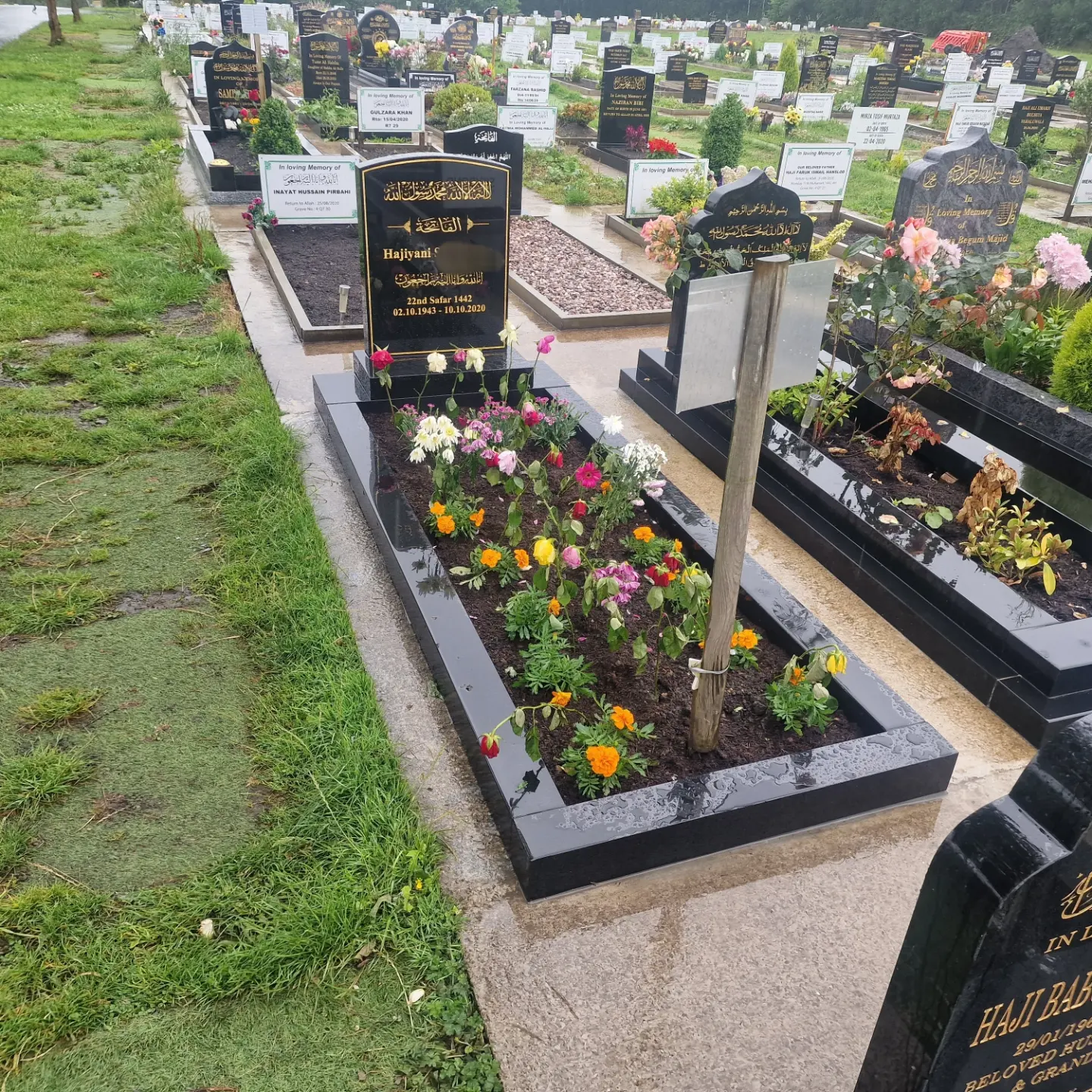 An installed arched memorial with gold lettering and flowers in a cemetery setting