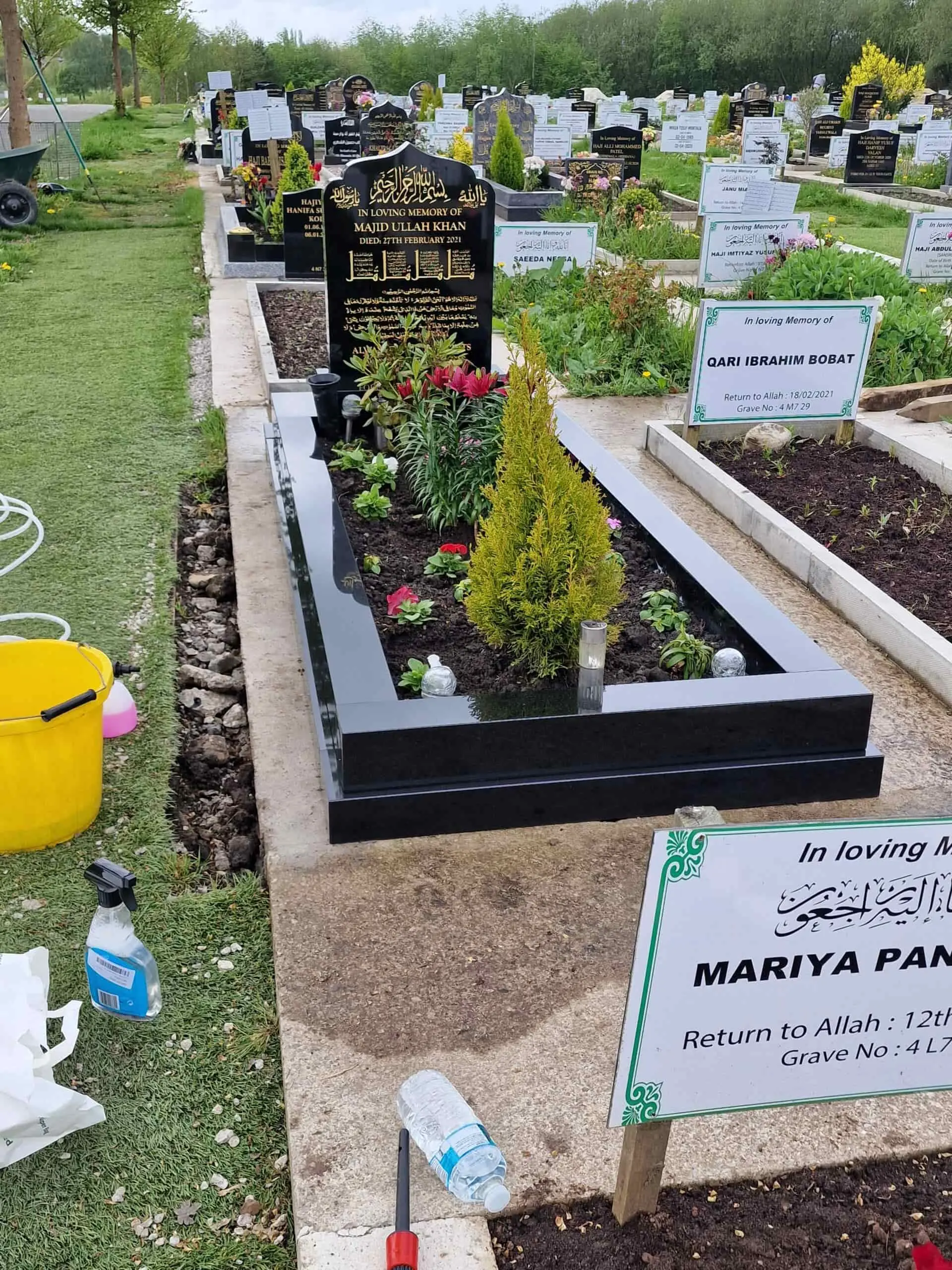 Polished black memorial with a shaped headstone, gold Arabic and English lettering, and a planted kerb surround